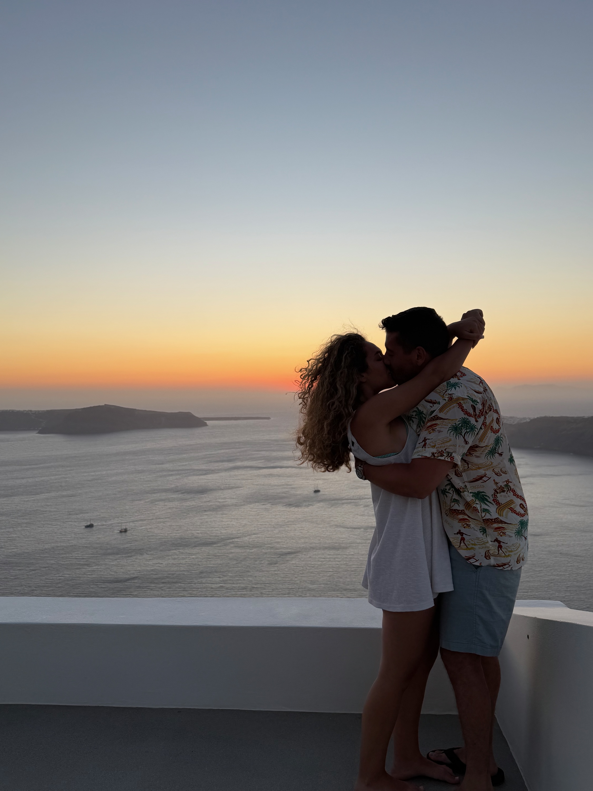 Foivos and Alexandra kissing above the Santorini caldera at sunset