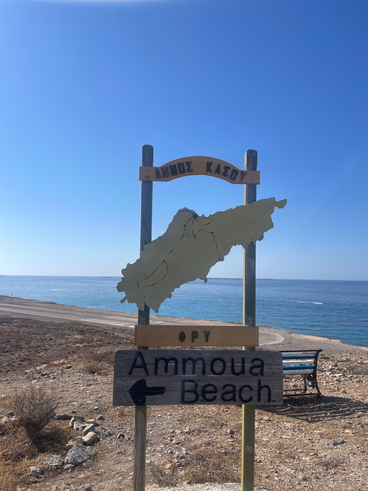 A wooden Kasos map and Ammoua Beach sign beside the sea